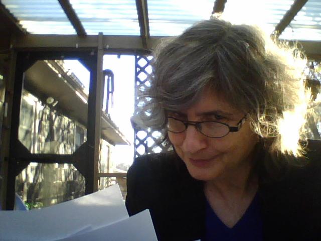 A woman peers over her glasses with a stern look, several typed pages in hand.